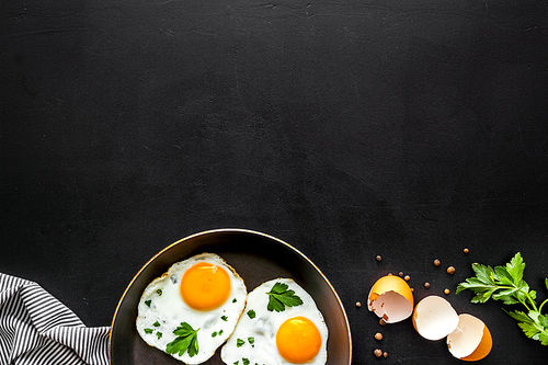 Fried eggs on frying pan on black background top view.