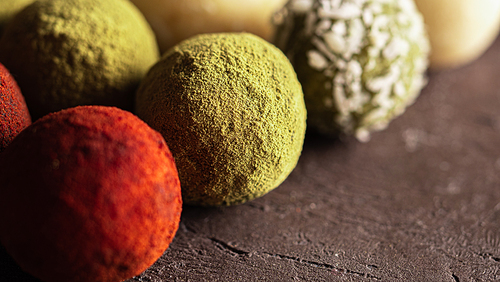 Colorful homemade truffles coated in dry beet powder, matcha tea powder, shredded cococnut on dark background. Copy space for text or design, banner.