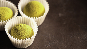 Homemade truffles candy with matcha tea powder in white paper cups on dark background. Copy space right for text or design. Shallow depth of field. Banner