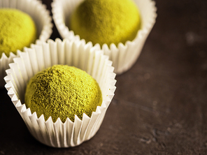 Homemade truffles candy with matcha tea powder in white paper cups on dark background. Copy space right for text or design. Shallow depth of field