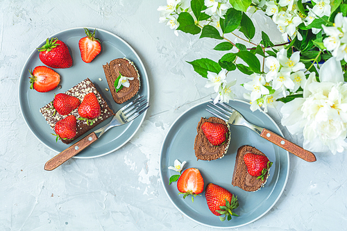 Chocolate rollcake with fresh strawberries on ceramic plate, jasmine and white peonies on light gray concrete surface table. Top view, flat lay, copy space for you text
