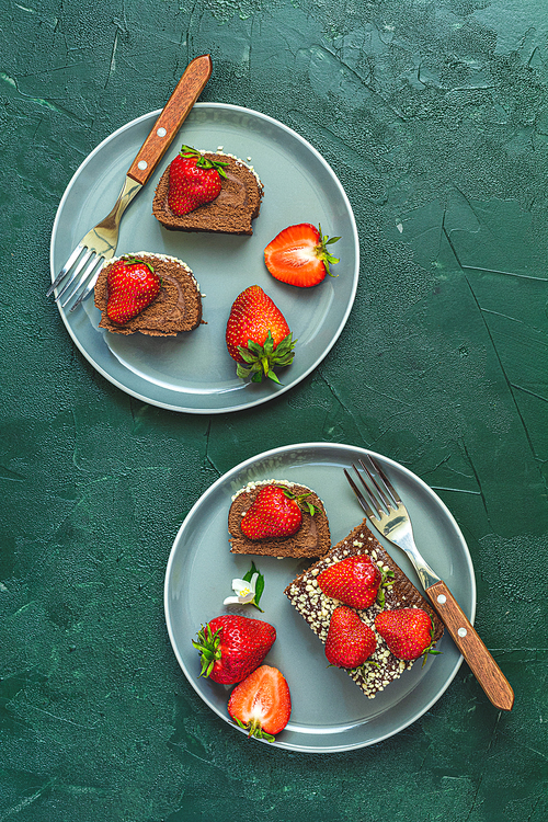 Chocolate rollcake with fresh strawberries in ceramic plate on dark green concrete surface table. Top view, flat lay, copy space for you text.