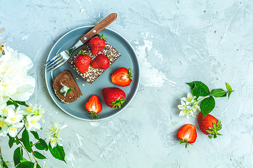Chocolate rollcake with fresh strawberries on ceramic plate, jasmine and white peonies on light gray concrete surface table. Top view, flat lay, copy space for you text.