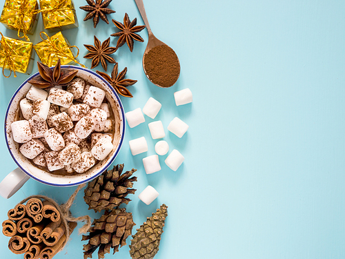 Cup of hot cocoa or carob or chocolate with marshmallow and winter spices and gifts on turquoise table top background. Flat lay with copy space. Christmas concept with copyspace
