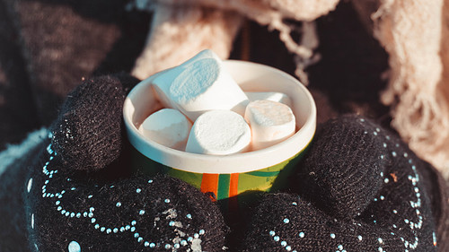A cup of cocoa with marshmallows in hands in mittens. Warm winter background. Warming drink.