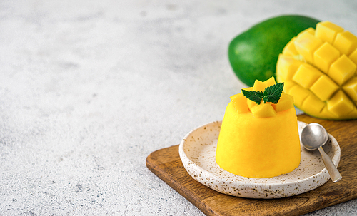 Mango Mousse on gray cement background with copy space left. Yellow mango mousse with sliced ripe mangoes. Banner.