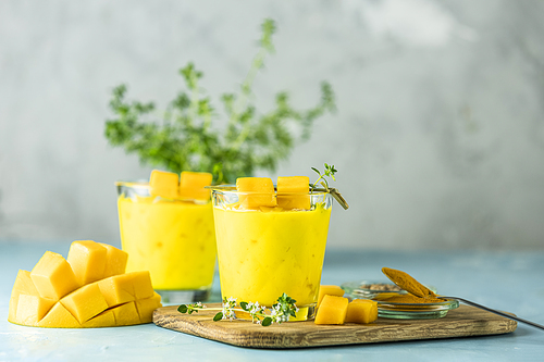 Yellow Indian mango yogurt drink Mango Lassi or smoothie with turmeric and saffron. Healthy probiotic Indian cold summer drink on blue background.