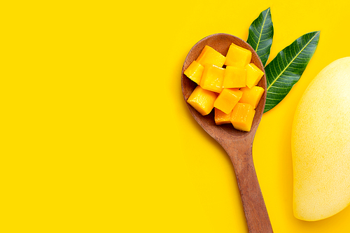 Sliced ripe mango cubes on wooden spoon on yellow background. Copy space