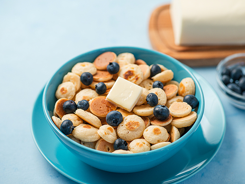 Trendy food - pancake cereal. Heap of mini cereal pancakes in boul on blue background. Copy space for text or design