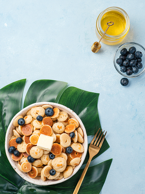 Trendy food - pancake cereal. Heap of mini cereal pancakes in boul on blue background. Copy space left for text. Top view or flat lay. Vertical.