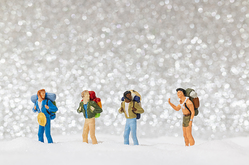 Miniature people: backpacker walking on snow background . Winter concept.