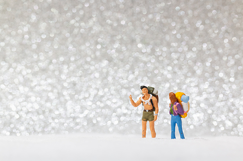 Miniature people: backpacker walking on snow background . Winter concept.