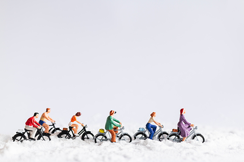 Miniature people : Travelers riding a bicycle on snow , winter background concept