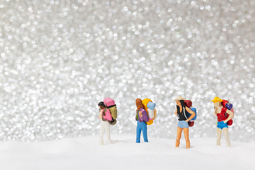 Miniature people: backpacker walking on snow background . Winter concept.