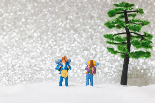 Miniature people: backpacker walking on snow background . Winter concept.