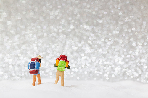 Miniature people: backpacker walking on snow background . Winter concept.