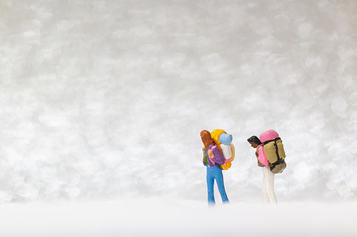 Miniature people: backpacker walking on snow background . Winter concept.