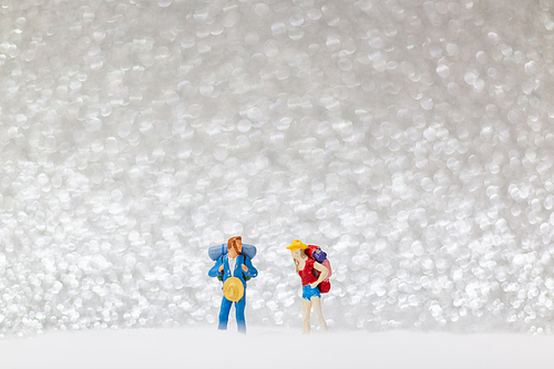 Miniature people: backpacker walking on snow background . Winter concept.