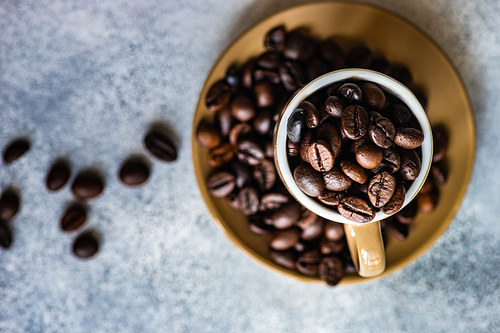 Cup full of organic coffee beans on stone background with copy space