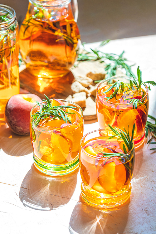 Glasses of sweet peach iced tea, Summer cold peach fizz cocktail with rosemary. Sunny light. Shallow depth of the field, close up, copy space for you text
