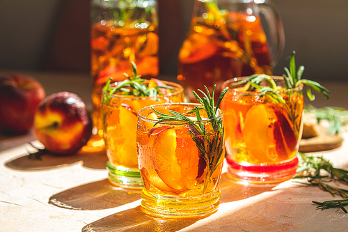 Glasses with drops of sweet peach iced tea, Summer cold peach fizz cocktail with rosemary. Sunny light. Shallow depth of the field, close up, copy space for you text