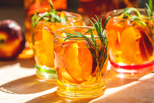 Glasses with drops of sweet peach iced tea, Summer cold peach fizz cocktail with rosemary. Sunny light. Shallow depth of the field, close up, copy space for you text