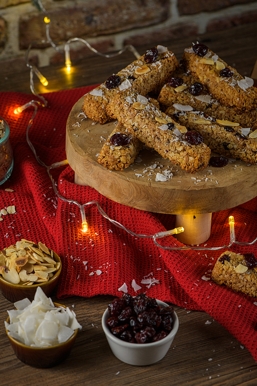 Cereal bars with almonds, coconut and cranberries on a Christmas season table decorated with lights.