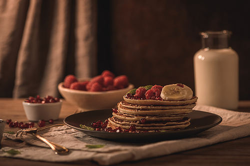 Pancakes with raspberries, banana slices, pomegranate seeds and honey on wooden vintage table.