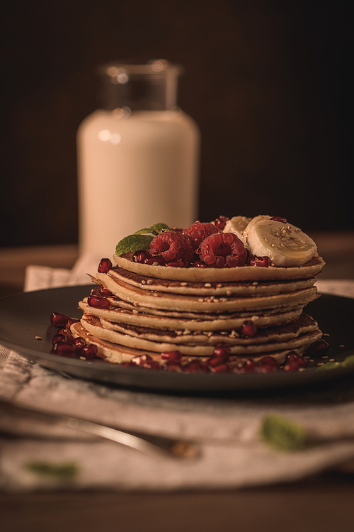 Pancakes with raspberries, banana slices, pomegranate seeds and honey on wooden vintage table.