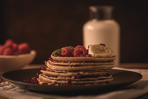 Pancakes with raspberries, banana slices, pomegranate seeds and honey on wooden vintage table.