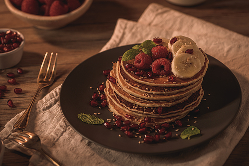 Pancakes with raspberries, banana slices, pomegranate seeds and honey on wooden vintage table.