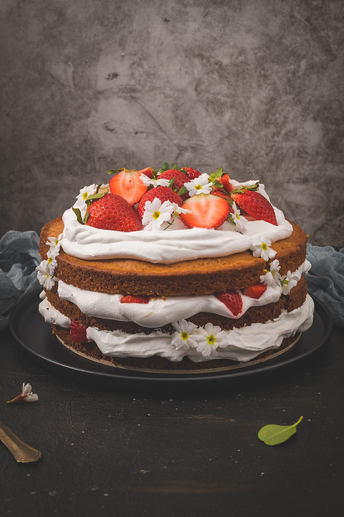 Strawberry cake, strawberry sponge cake with fresh strawberries and sour cream on a dark kitchen countertop.