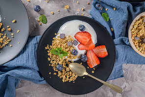 Ripe blueberries and strawberries with yogurt and granola in plate on a light grey background. Healthy Eating.