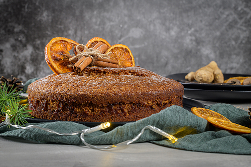 Christmas orange cake decorated with dried oranges on Christmas decorated kitchen countertop.