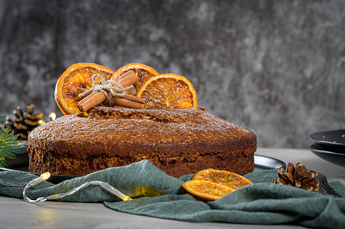 Christmas orange cake decorated with dried oranges on Christmas decorated kitchen countertop.