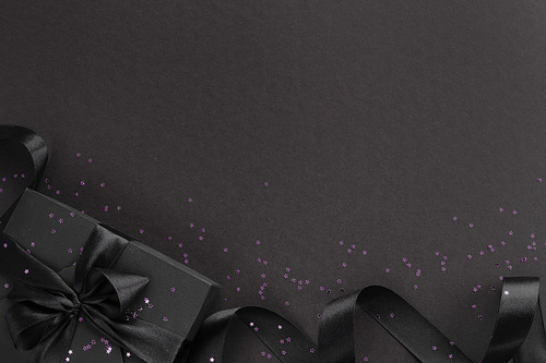 Black friday gift, paper box with silk ribbon bow and purple glitter stars on black paper background with copy space for text, flat lay top view template