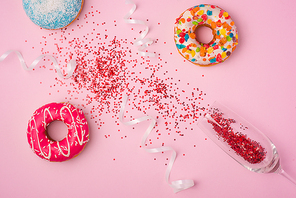 Flat lay of Celebration. champagne glass with colorful party streamers and delicious donuts on pink background.