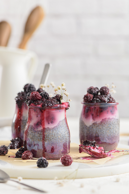 Chia pudding with blackberries, three portions in glass jars on a white table.