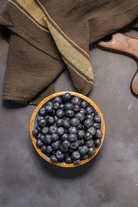Fresh blueberries in ceramic bowl and brown cloth on dark table, rustic style.