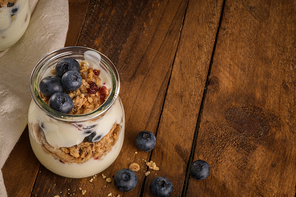 Yogurt parfait with blueberry and granola. Healthy breakfast concept served in mason jar with decorative spoons on wooden table.