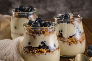 Yogurt parfait with blueberry and granola. Healthy breakfast concept served in mason jar with decorative spoons on wooden table.