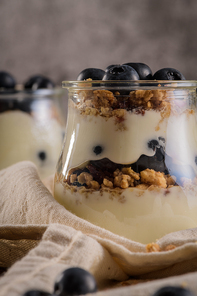 Yogurt parfait with blueberry and granola. Healthy breakfast concept served in mason jar with decorative spoons on wooden table.