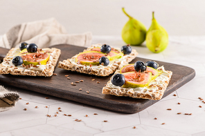 Canape or crostini with multigrain  crispread with cream cheese and fresh fig slices on a wooden board. Delicious appetizer ideal as an aperitif.