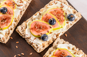 Canape or crostini with multigrain  crispread with cream cheese and fresh fig slices on a wooden board. Delicious appetizer ideal as an aperitif.