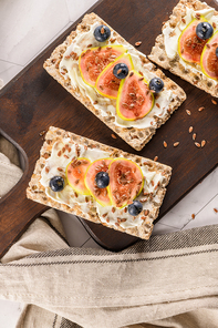Canape or crostini with multigrain  crispread with cream cheese and fresh fig slices on a wooden board. Delicious appetizer ideal as an aperitif.