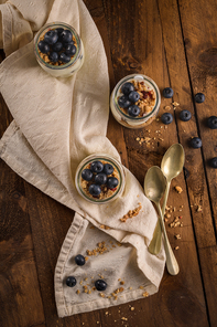 Yogurt parfait with blueberry and granola. Healthy breakfast concept served in mason jar with decorative spoons on wooden table.