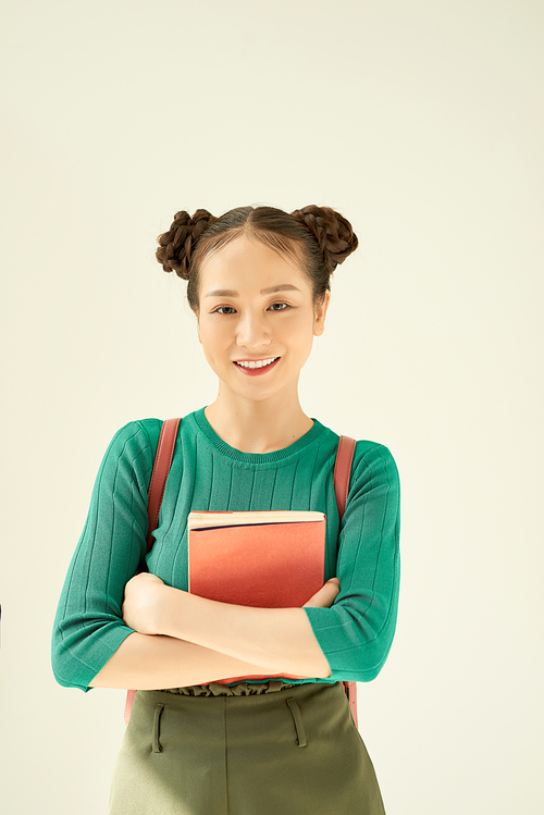 Portrait of a cheerful pretty asian girl holding books and  isolated over light background