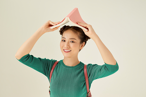 Asian young woman happy and smile holding open book on head on light background