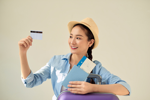 Happy tourist woman holding credit card, passport tickets isolated on gray background. Female traveling abroad to travel on weekends getaway. Air flight concept