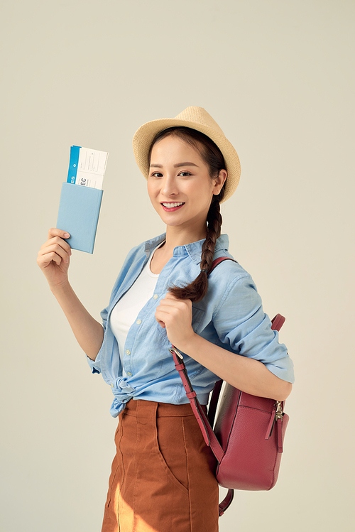 Portrait of a cheerful cute asian girl traveller showing passport with tickets isolated over gray background
